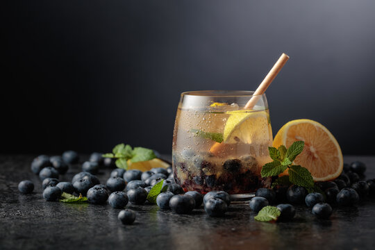 Iced blueberry drink with mint, lemon, ice, and fresh berries on a black stone table.