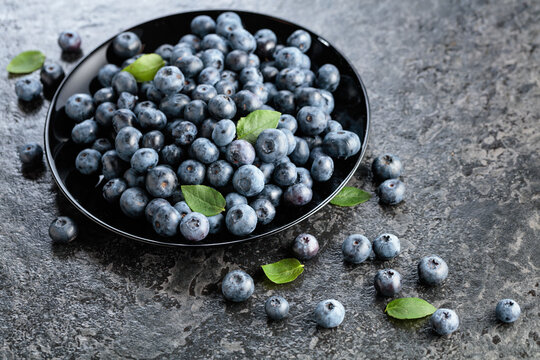 Blueberries with their leaves on a black plate.