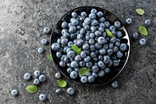 Blueberries with their leaves on a black plate.