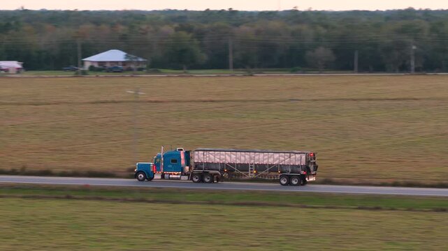 Rural highway traffic with semi truck transporting freight at fast speed, setting sun illuminating road ahead. Safety, supply chain and cargo movement concept.