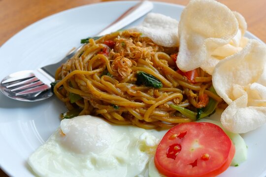 Colse up Fried Noddles or Mie Goreng on plate, served with sunny side up egg, sliced tomato, and crackers