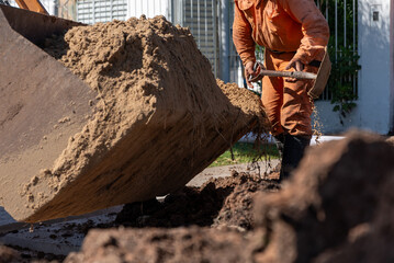 Construction worker using shovel to spread sand unloaded from excavator bucket © MatiasLeonel