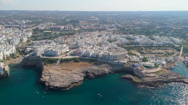 Aerial view of rocky promontory with historic white town of Polignano a Mare and shallow turquoise water sparkling along the coastline