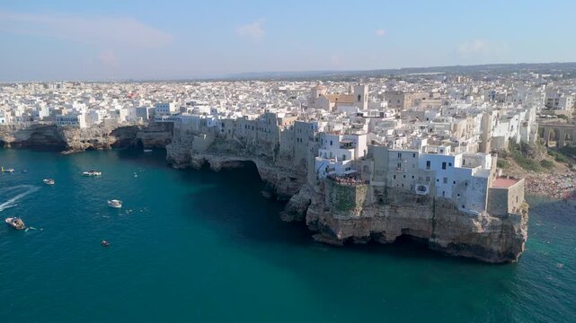 Aerial view of boats sailing on blue Adriatic sea along limestone cliffs with white town of Polignano a Mare on the coastline