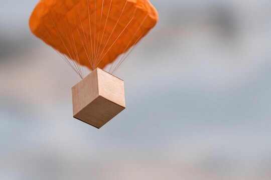 Orange parachute gently lowers a wooden box through the sky, symbolizing safe delivery and careful logistics.
