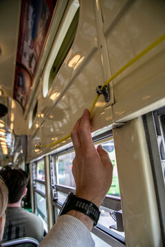 Passenger's hand pulling the yellow stop-request cord inside a classic public transit vehicle, such as a San Francisco cable car or historic streetcar. The flexible yellow chime cord runs along train