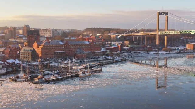 Aerial view of the Alvsborg Bridge spanning the icy waters of the Gota Alv river with snow-covered industrial buildings and boats in Gothenburg, Vastra Gotaland County, Sweden.