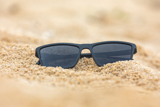 Close-up of black sunglasses partially buried in soft beach sand, capturing a relaxed summer vibe and outdoor leisure concept.