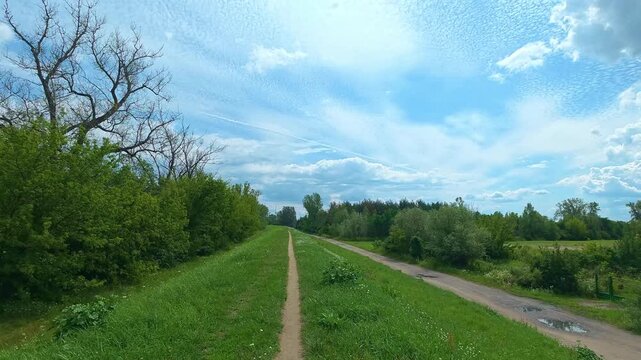 Rural trail stretching along green embankment beside dirt road. Bicycle POV
