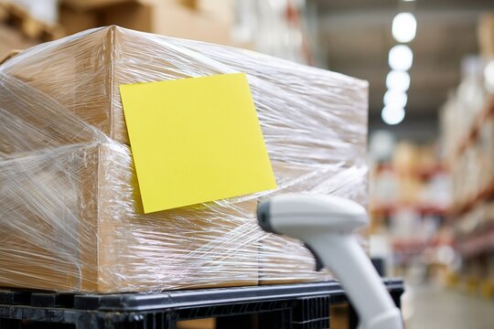 Cardboard box wrapped in plastic with yellow label being scanned by barcode reader in warehouse