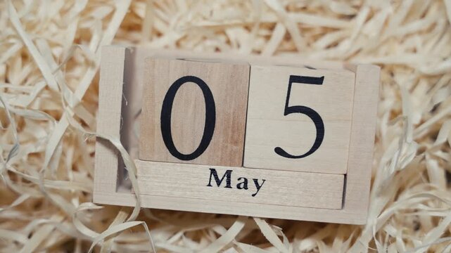 Wooden calendar blocks showing date May 5 on natural wood shavings background