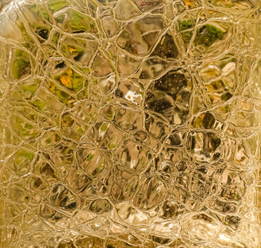Square close-up of golden textured glass with irregular reflections, abstract luxury background with warm translucent surface