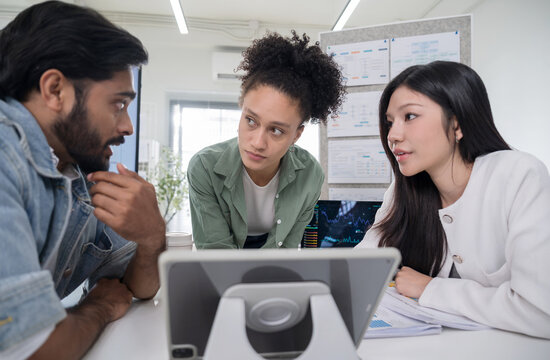 Close up of three corporate professionals gathering around a digital tablet, looking seriously at the screen to solve a problem and discuss business strategy.