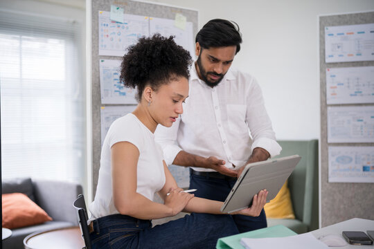 Professional business colleagues collaborating closely in the office, with a manager leaning over a desk to review project data on a laptop with a female team member.