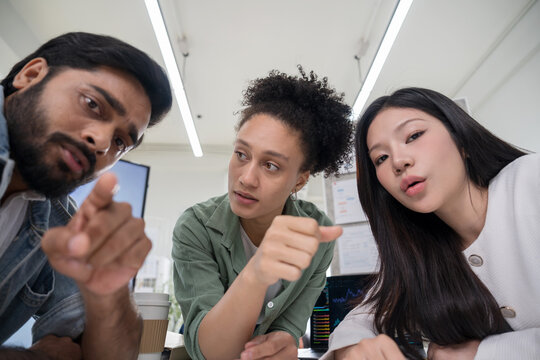 Close up of three corporate professionals gathering around a digital tablet, looking seriously at the screen to solve a problem and discuss business strategy.
