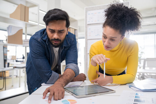 Male and female professionals analyzing business data and discussing strategy over a digital tablet and documents in a modern workspace.