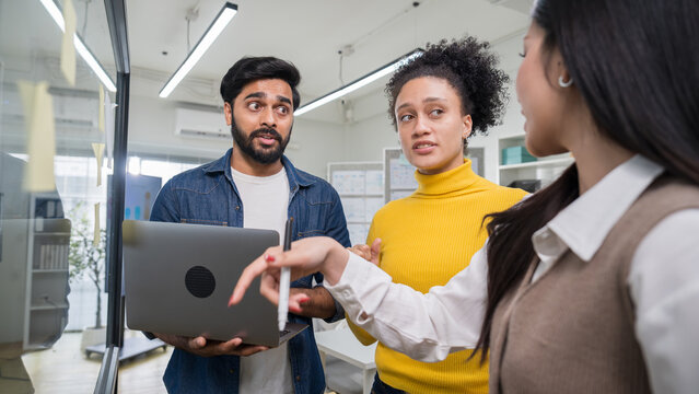 Male professional holding a laptop and collaborating with a female colleague, discussing digital project updates in a modern office environment.