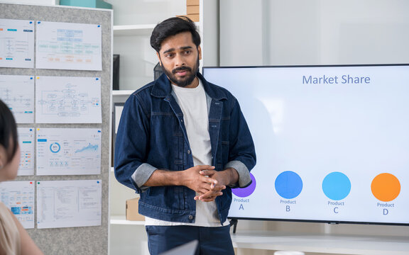 Professional businessman standing in front of a digital screen, presenting market share graphics and business development plans to his team.
