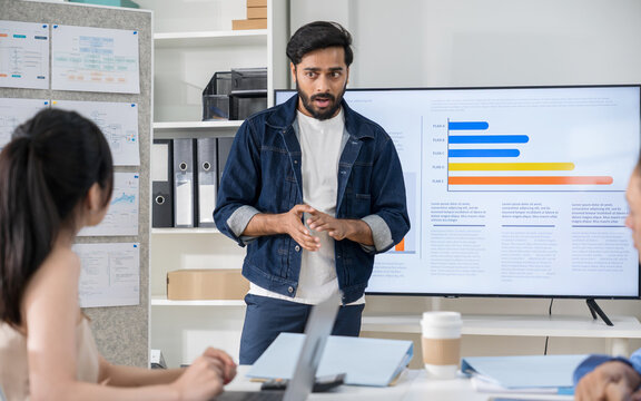 Confident male manager leading a strategy meeting, presenting financial bar charts on a digital display to team members at the boardroom table.