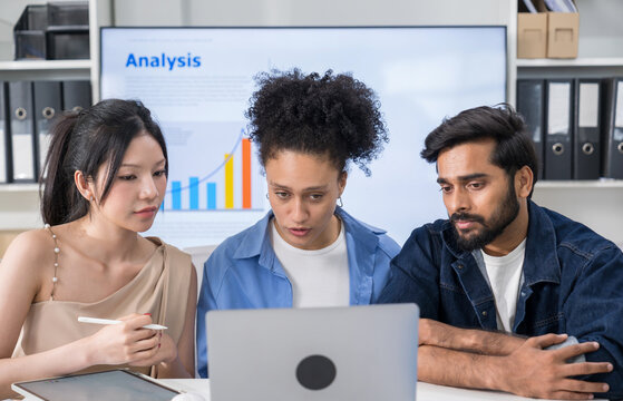 Three professional colleagues looking at a laptop screen together, discussing project details during an online video conference with a client.