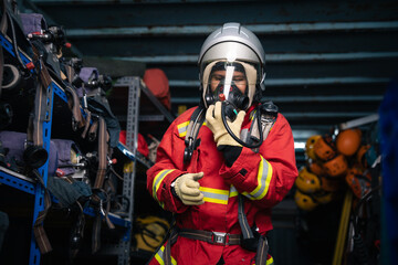 Fototapeta premium Firefighter in Full Protective Uniform Giving a Thumbs-Up Gesture while Adjusting a Face Mask inside an Equipment Storage Area