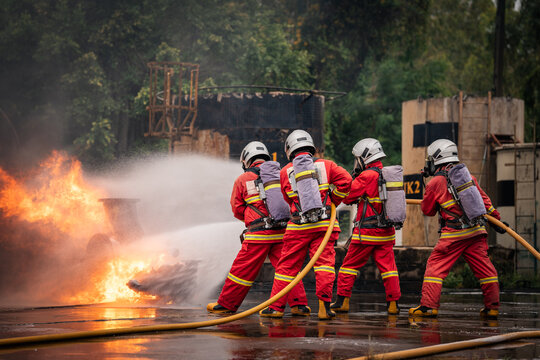 Firefighter Team Fighting an Industrial Fire with a Powerful Hose Stream while Wearing Full Protective Uniforms and Air Tanks