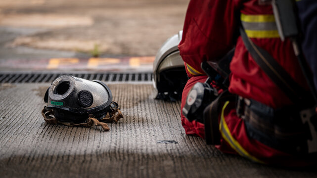 Firefighter Equipment with a Full Face Respirator Mask Resting on Wet Pavement beside a Helmet and Red Protective Uniform