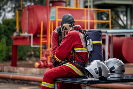 Firefighter Team Gathered beside Protective Helmets while Wearing Red Reflective Uniforms and Air Tanks at an Industrial Site