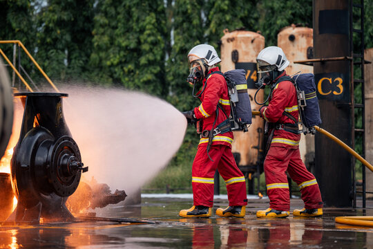 Firefighter Team Directing a Powerful Hose Stream toward Burning Industrial Equipment while Wearing Full Protective Uniforms