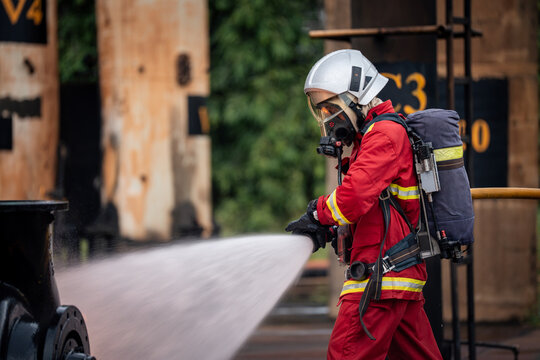 Firefighter Operating a Fire Hose Nozzle toward Industrial Equipment while Wearing a Full Face Mask, White Helmet, and Air Tank