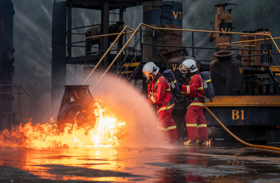 Firefighter Team Battling an Industrial Fire with a Hose while Wearing Full Protective Uniforms, Face Masks, Helmets, and Air Tanks
