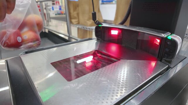 Customer scanning bag of fresh red apples at self checkout station