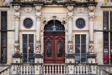 Fototapeta premium Facade with ornate stone columns and sculptures. Facade around an antique wooden entrance. Historic building facade with gilded architectural details. European architecture with facade.