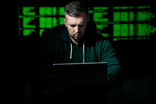 Hacker types code on laptop keyboard. Hacker analyzes system vulnerability at night. Hacker monitors server and database access. Hacker launches cyber attack on network.