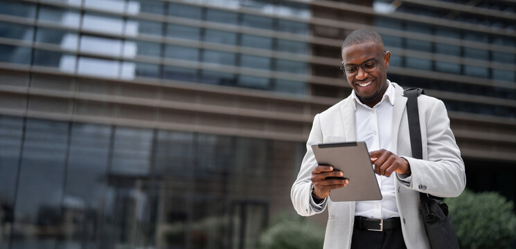 Using tablet, scrolling report, african american businessman outdoor near office building, works as marketing director. Black business man smiling, reviewing project details. Copy space. Web banner.