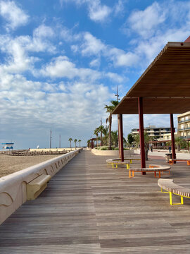 A serene beach boardwalk with a covered seating area under a blue sky
