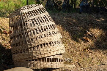 Stacked traditional woven bamboo chicken cages sitting on dry ground outdoors. Agriculture and poultry equipment concept in horizontal view. © panji