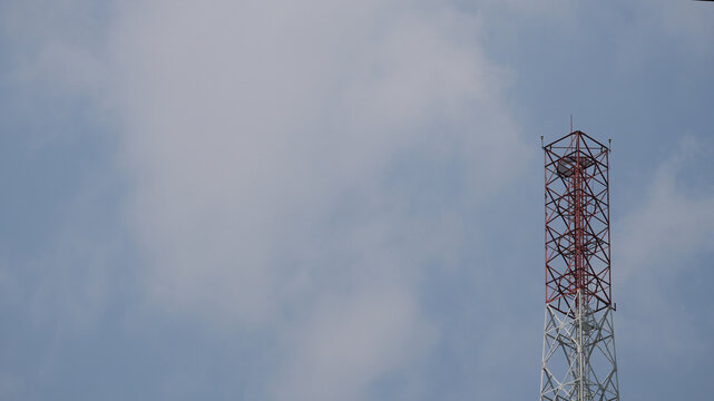 Telecommunication tower with red and white patterns against a cloudy blue sky background