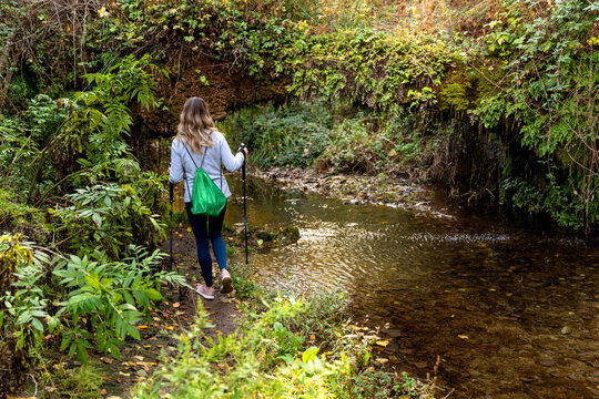 Woman enjoying nordic walking on autumn forest path next to flowing river