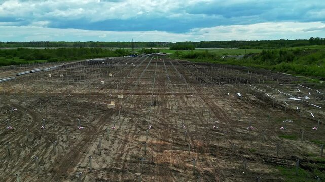 Aerial view of a large solar farm construction site with rows of metal posts and wooden crates in a rural field in Latvia.