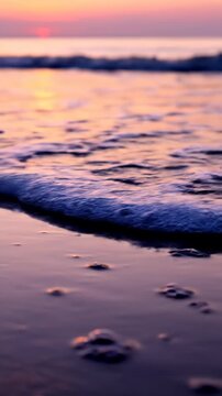 Calm ocean waves washing onto a sandy beach during a vibrant pink and purple sunset.