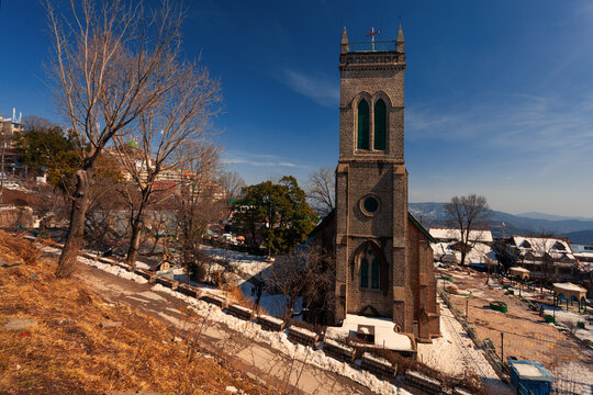 View of the historic Holy Trinity Church surrounded by snow-covered grounds and trees under a clear blue sky in Murree, Punjab, Pakistan.