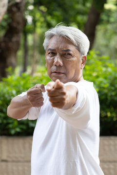 asian senior man practicing baduanjin qigong in an urban park, drawing the bow to shoot eagle pose for shoulder strength and flexibility, tired and serious mood