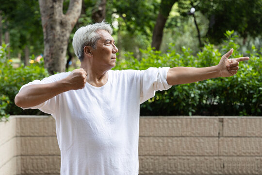 asian senior man practicing baduanjin qigong in an urban park, drawing the bow to shoot eagle pose for shoulder strength and flexibility, tired and serious mood