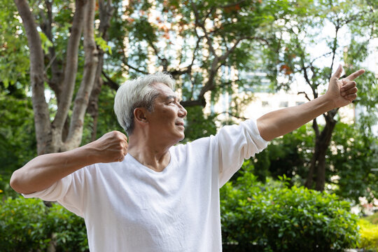 asian senior man practicing baduanjin qigong in an urban park, drawing the bow to shoot eagle pose for shoulder strength and flexibility, with relaxed smiling happy mood