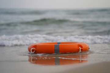 Orange life ring rests on wet sand. Ocean waves roll gently behind it. Soft light reflects off its surface. Stillness hints at safety or rescue. Perfect for coastal safety or beach themes © polack