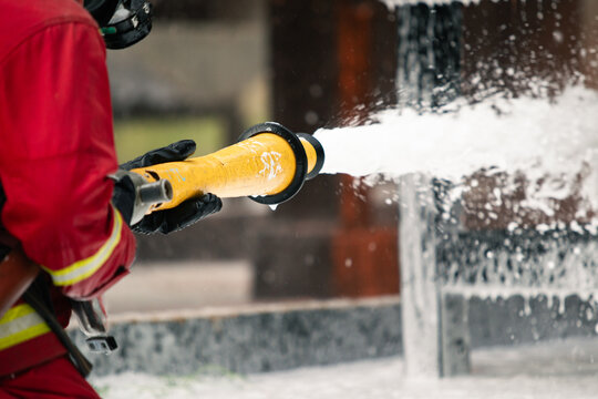 Firefighter spraying firefighting foam from hose onto industrial building