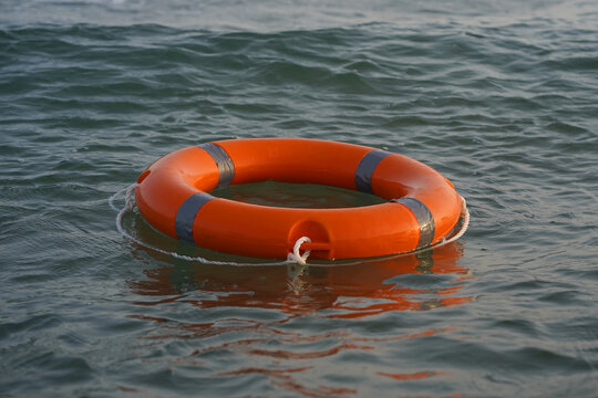 Orange life ring floats gently in calm water in sea. Ripples surround it, reflecting sunlight. It signals safety, rescue, or emergency readiness