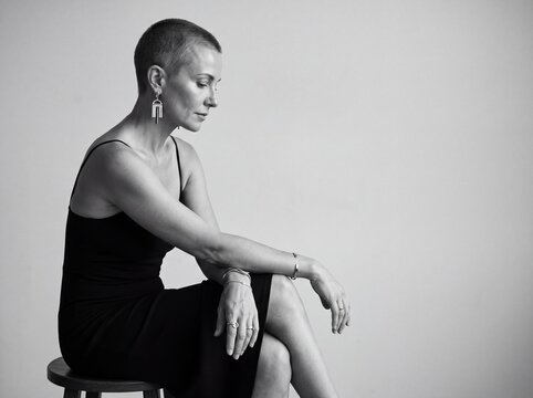 Woman in a black dress: A thoughtful woman with a shaved head sits elegantly, her expression contemplative. The black and white portrait captures a mood of quiet introspection.