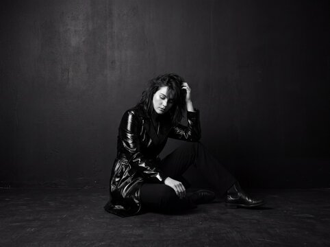 Melancholy Mood: A lone individual sits in a contemplative pose, head bowed and hand to their brow, exuding a palpable sense of sadness and introspection against a stark, dark backdrop.
